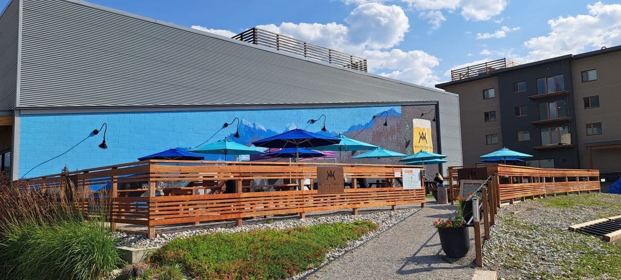 Blue umbrellas and a mountain mural create an inviting ambiance at Whitetooth Brewing Co.'s massive outdoor patio in Golden BC Canada