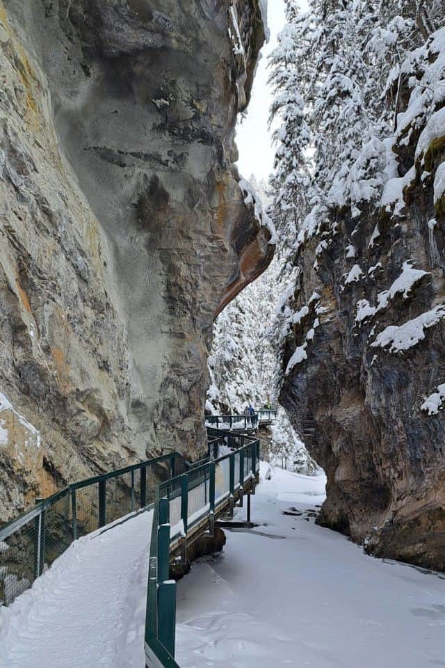 A snowy catwalk weaves its way around a rockface as it squeezes through a narrow passage on the Johnston Canyon Trail in Banff Alberta Canada