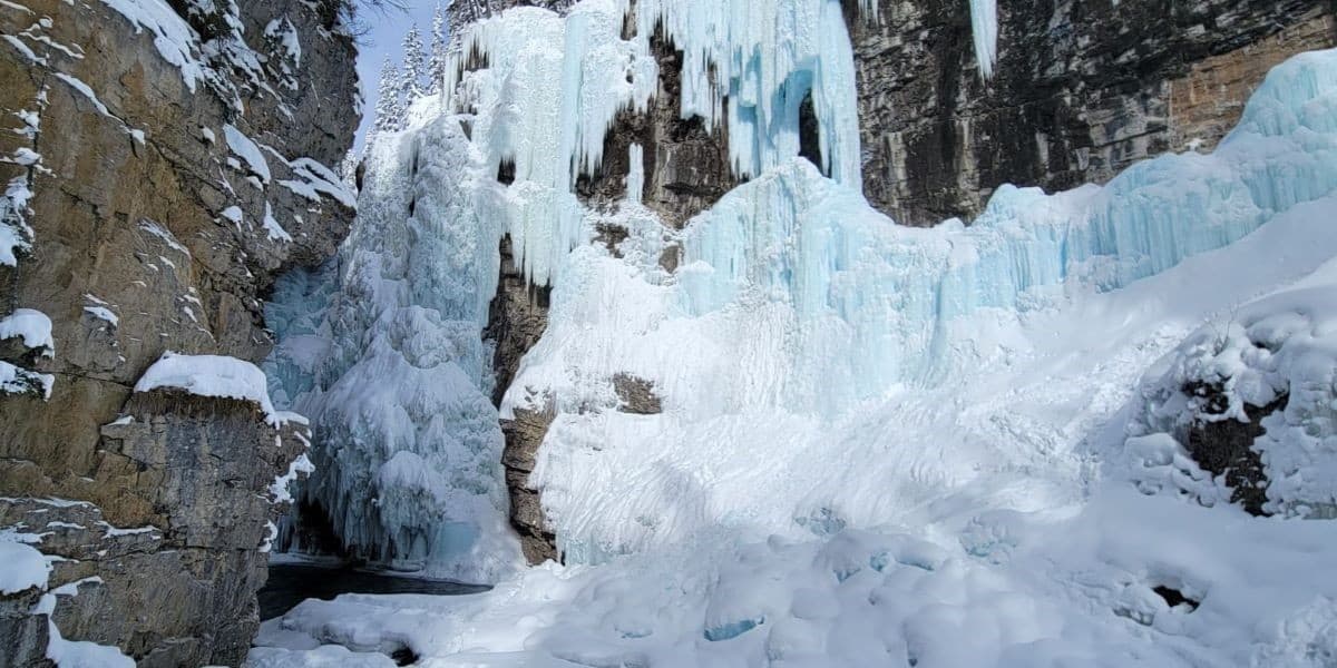 An icy blue frozen waterfall clings to the rockface at Johnston Canyon in Banff National Park AB.