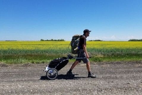A hiker pulls a cart along open prairie roads on the Crow Wing Camino in Manitoba, highlighting the vast landscapes, solitude, and immersive long-distance walking experience of this Canadian pilgrimage trail.