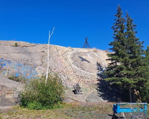 Cultural Crossroads is a public art piece that greets visitors to Old Town Yellowknife. There are hundreds of handprint etched into the rock face along with a raven flying within a white circle towards the frame of a tipi on the top of the rock.