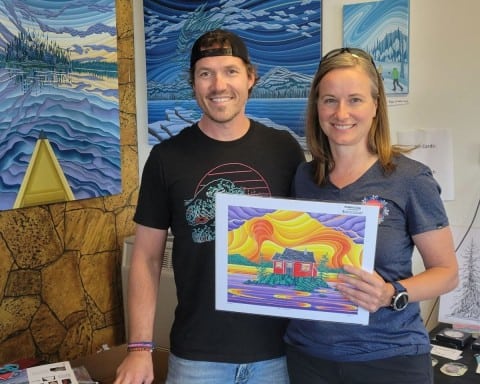 Janet Guthrie, Canada Adventure Seeker poses with Yellowknife artist, Robbie Craig in his studio in Old Town. The two are holding one of his prints.