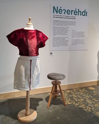 An Indigenous fashion designer displays a modern dress with a red top and a white skirt made out of seal skin and using traditional Frist Nations techniques.