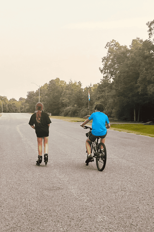 Two teens being active outdoors. One girl is rollerblading and one boy is riding his bicycle.