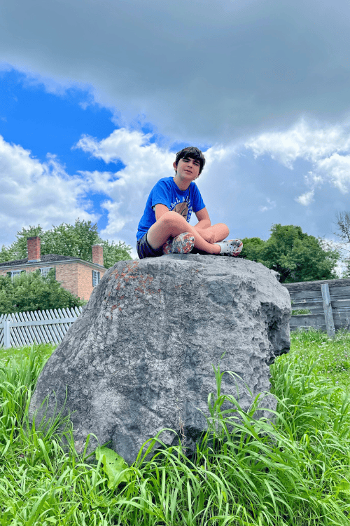 A Canadian Guide for Travelling with Type 1 Diabetes (T1D). Boy sits on a rock in a grass field on a cloudy day.