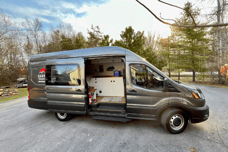 A large, grey,  camper van parked in a driveway with the sliding door open to reveal the kitchen inside