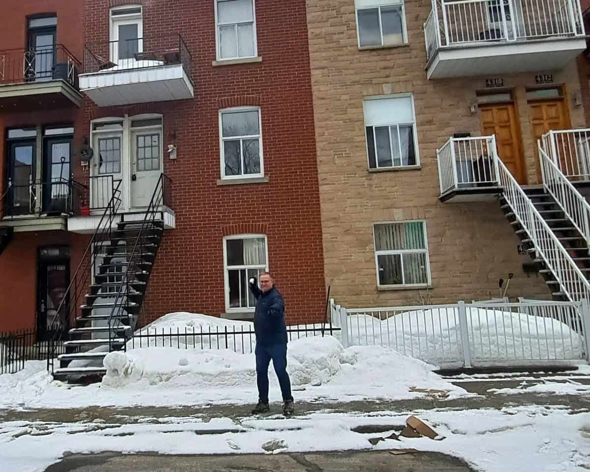 Standing in front of typical Montreal  townhouses in the Le Plateau area of the city, a man takes aim with a snowball in hand. In Montreal, playing in the snow is also one of the attractions and a faourite activity amongst locals.