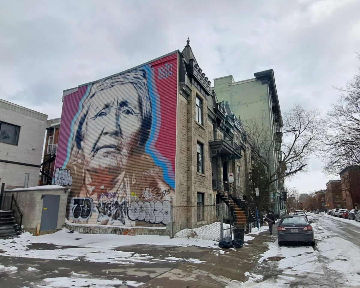 A 3-story high mural os an elderly First Nations Lady is painted on the side of a traditional Montreal-style townhouse in the Le Plateau region of the city.