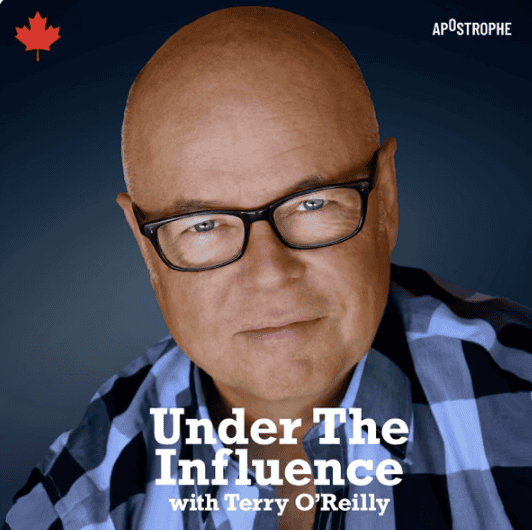 Terry O'Reilly wearing dark rimmed glasses looks thoughtfully at the camera wearing a plaid shirt.