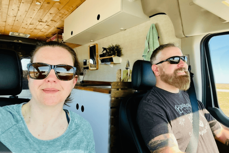 Smiling man and woman travelling through the Canadian prairies in a camper van