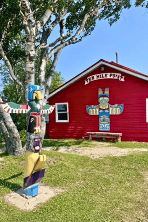 Wooden structure painted in bright red, with an image of a totem pole on the side of the building under the white sign that reads 