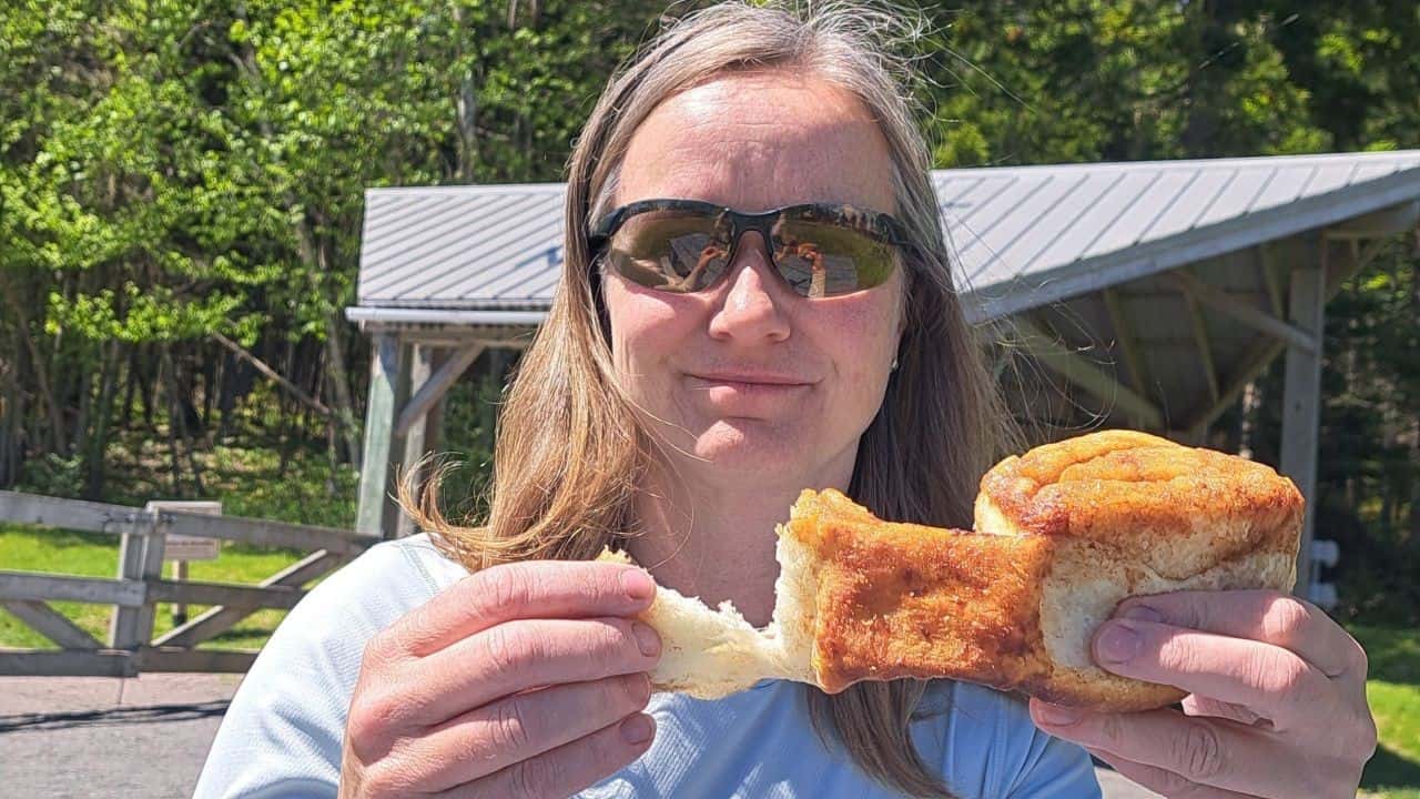 Traveler enjoying a world famous sticky bun from Kelly’s Bakeshop in Alma, New Brunswick, during a picnic lunch at Hopewell Rocks Provincial Park by the Bay of Fundy.