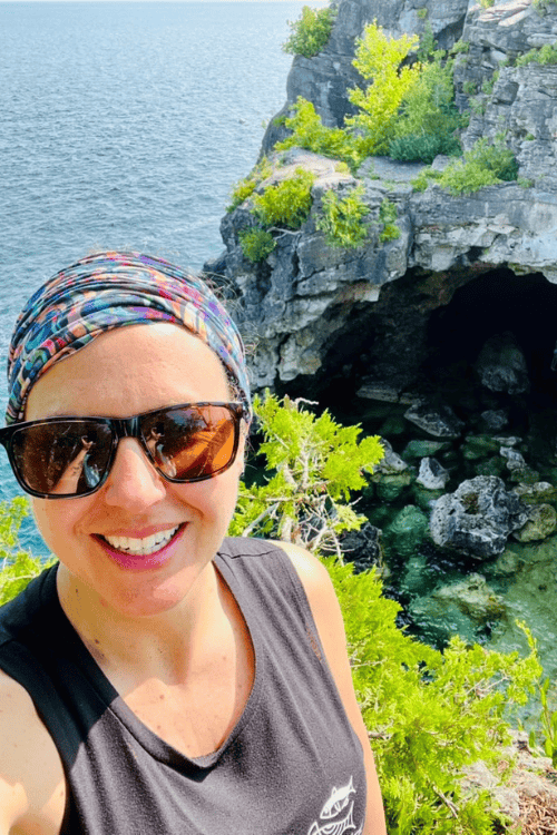 A woman smiles with sunglasses, in front of the Grotto at Bruce Peninsula National Park.