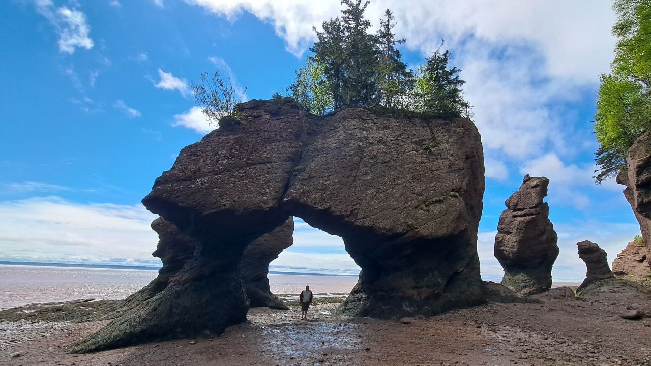 A man stands on the ocean floor underneath giant rock formations during low tide at Hopewell Rocks Provincial Park in New Brunswick Canada.