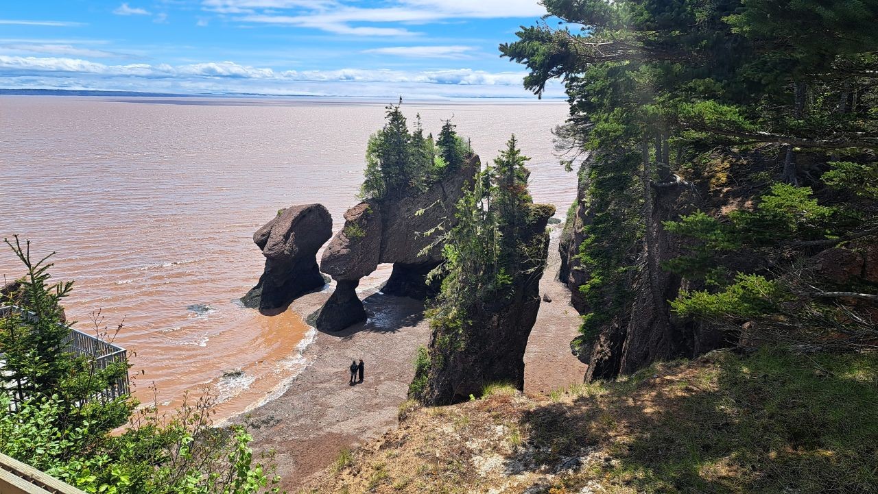 A couple walks amongest the flower pot rocks on the muddy ocean floor during low tide at Hopewell Rocks in the Bay of Fundy in New Brunswick.
