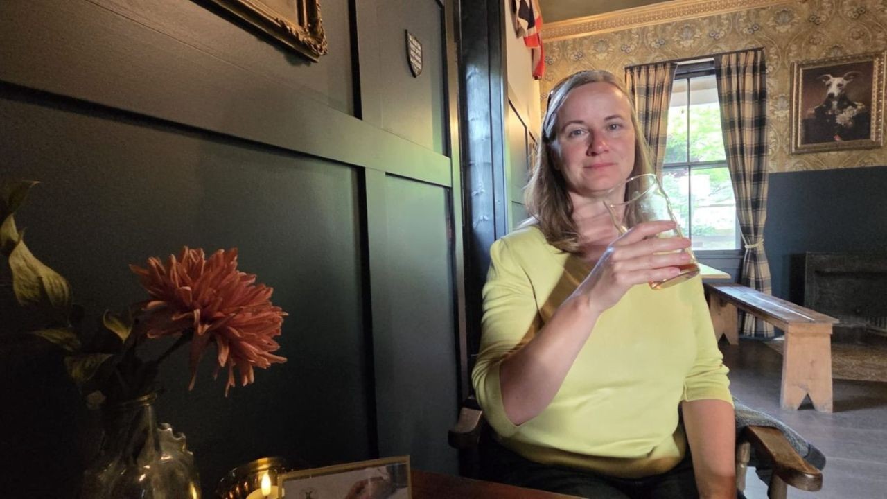A lady enjoys a pint of beer in The Thirsty Whippet English Pub in Dorchester New Brunswick Canada. Behind her is a framed painting of a whippet dressed as British royalty.