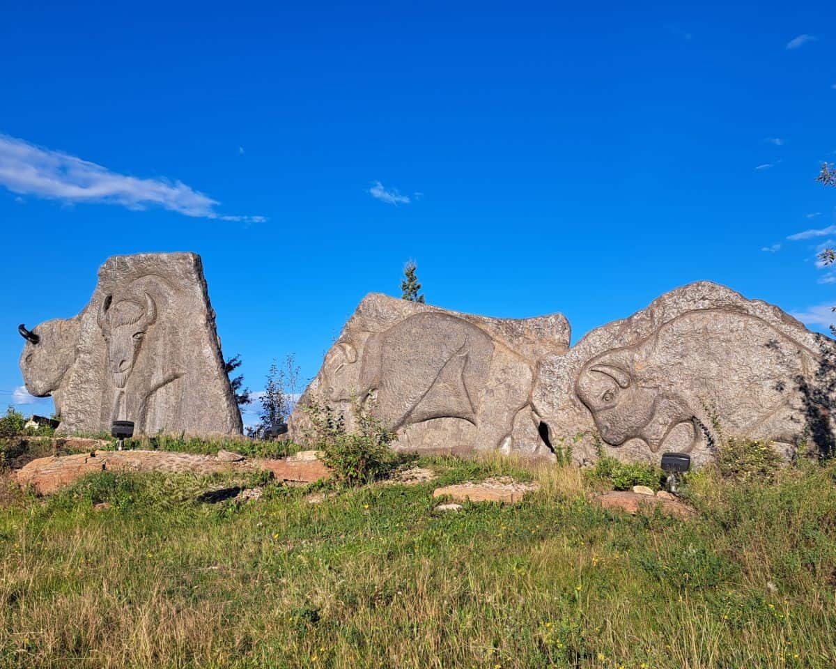 A massive stone carving of a herd of buffalo set against a clear blue sky