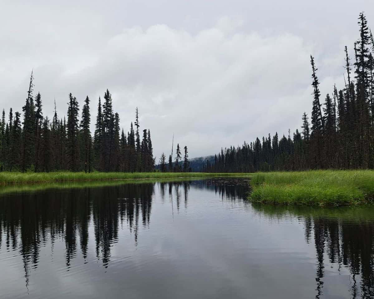 Overcast skies on Kibbee Lake's calm waters reflect the trees along the shoreline.
