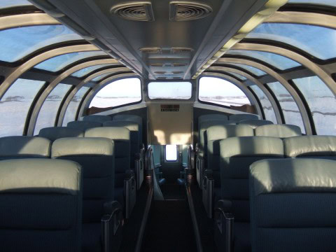 Passengers gather in the panoramic dome car aboard VIA Rail’s The Canadian, watching winter Prairie skies, snow fences, and distant horizons glide past during a relaxed day of cross-country train travel.