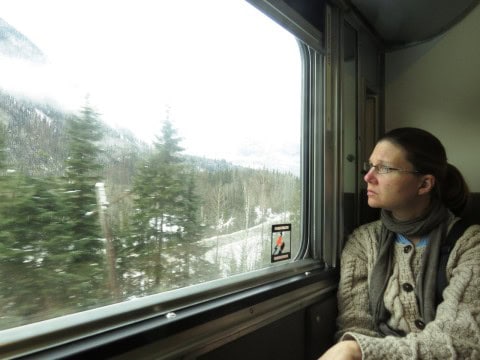 A passenger gazes through the snow-dusted window of VIA Rail’s The Canadian, capturing the quiet beauty of forests, lakes, and mountains — an intimate reflection of slow train travel across wintery Canada.