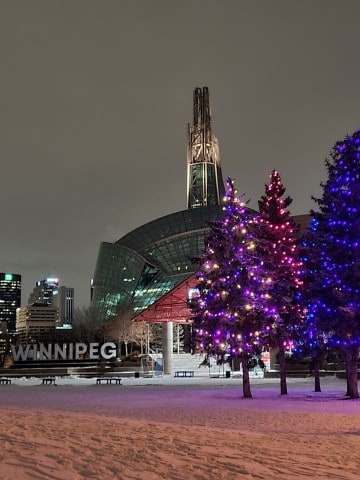 Christmas lights illuminate The Forks Market in Winnipeg on a winter evening, creating a festive atmosphere during a brief stop while traveling across Canada by train aboard VIA Rail’s The Canadian.