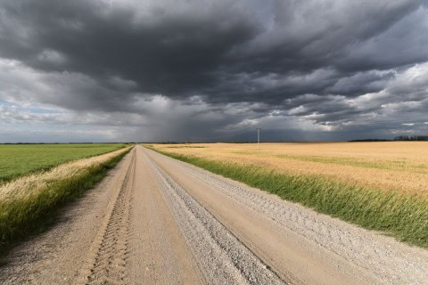 A gravel road beneath dramatic prairie skies reflects the Trans Canada Trail’s vast central routes, where open landscapes, changing weather, and long distances define travel across Saskatchewan and Manitoba.