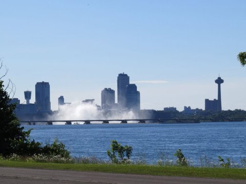 View of Niagara Falls cityscape with mist rising from the falls along the Niagara River Recreational Trail in Ontario, Canada, capturing the iconic waterfalls, urban skyline, and surrounding natural atmosphere.