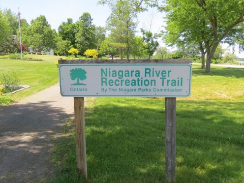 Trail sign and paved pathway along the Niagara River Recreational Trail in Ontario, Canada, guiding hikers and cyclists through scenic riverfront landscapes with accessible, well-marked routes for outdoor exploration.