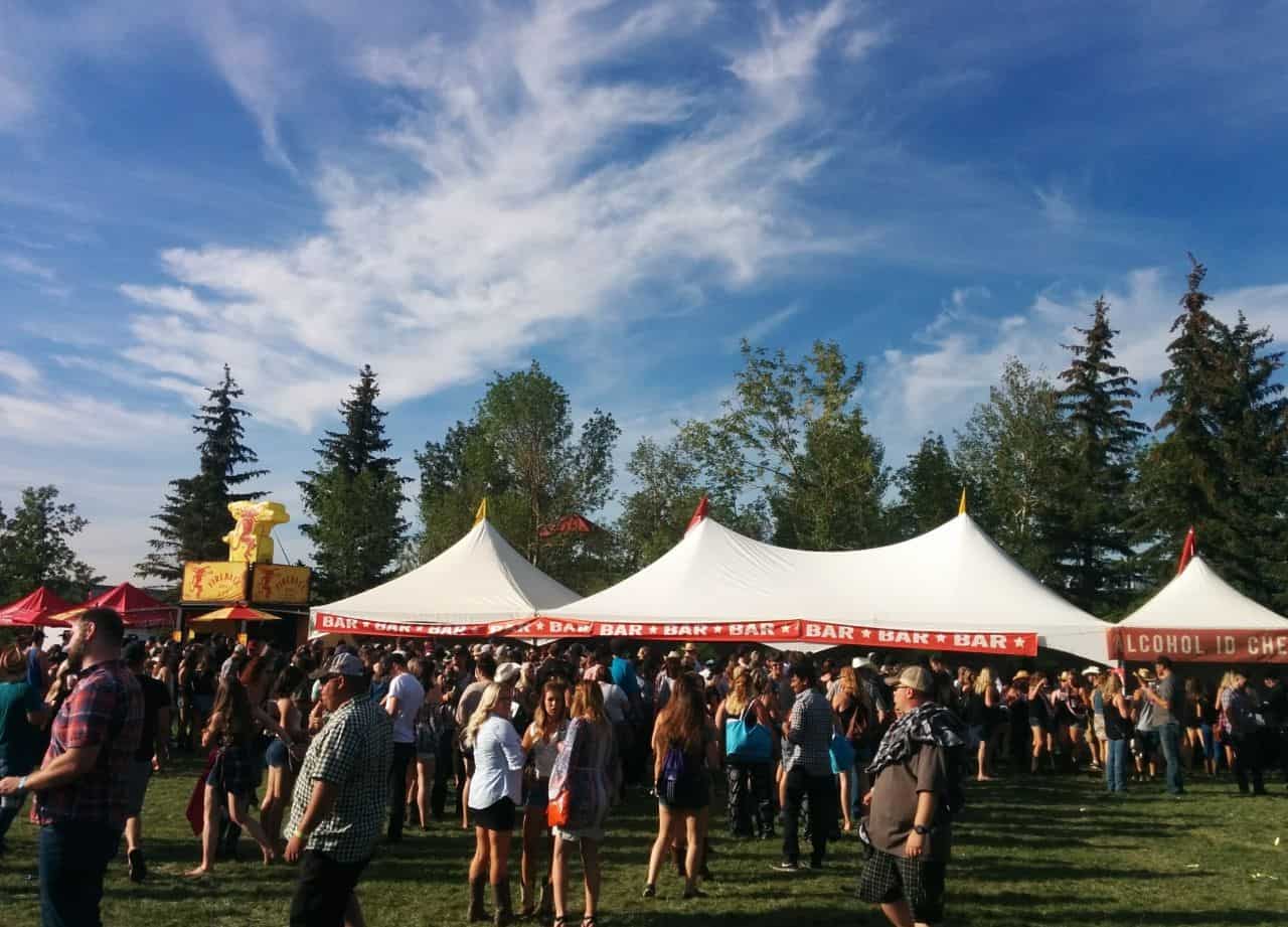 people walking near bar tents at outdoor summer music festival in Western Canada