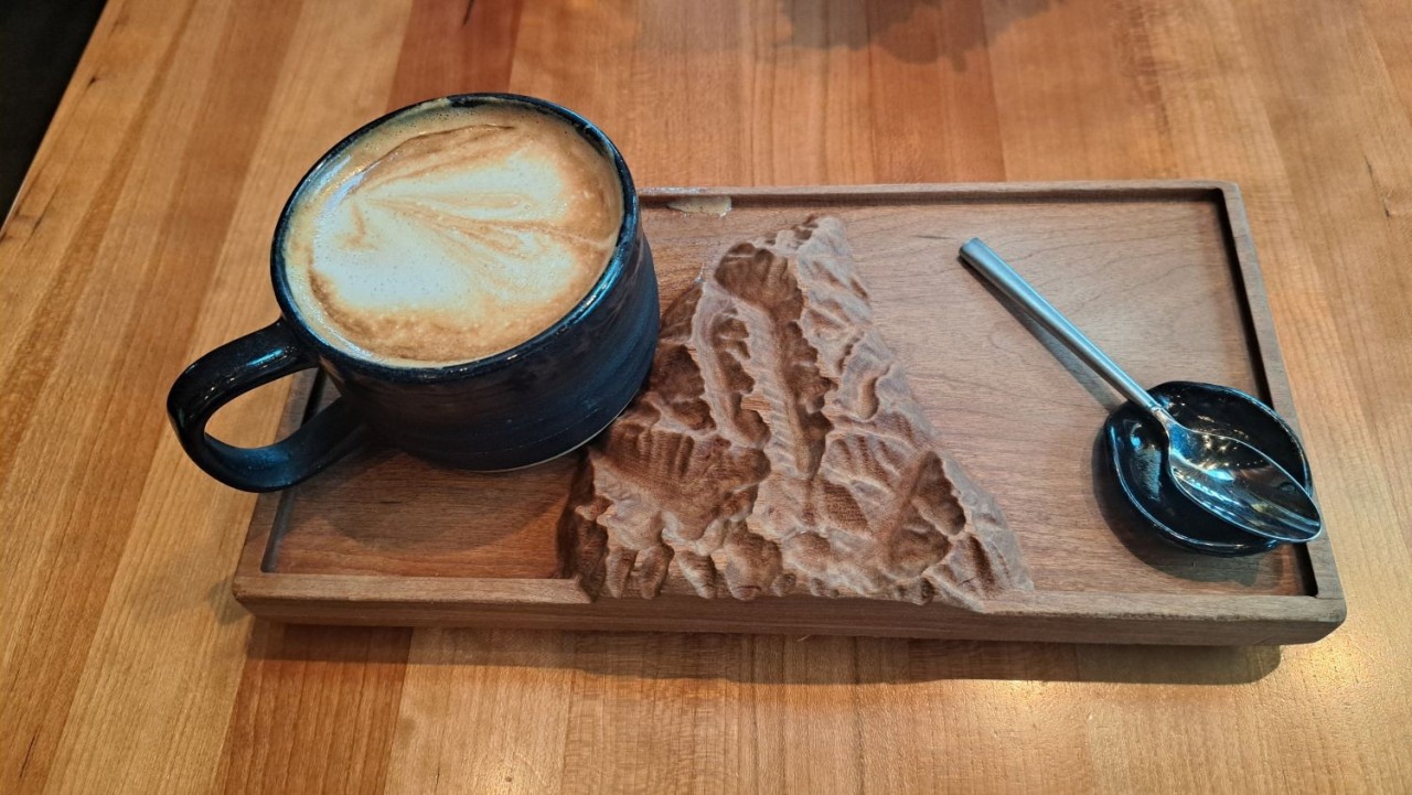 Latte at Kicking Horse Café Invermere BC – Signature Roastery Coffee Experience - A handcrafted latte at Kicking Horse Café in Invermere, BC, served on a wooden platter with signature mountain design. A distinctive roastery experience highlighting bold, organic, fairtrade coffee.